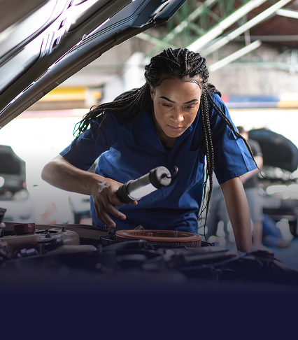 A mechanic looking under the hood of a vehicle with a light