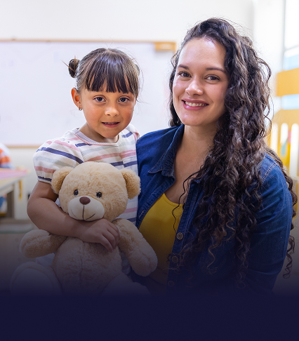 A smiling woman sitting with a child holding a teddy bear on her lap